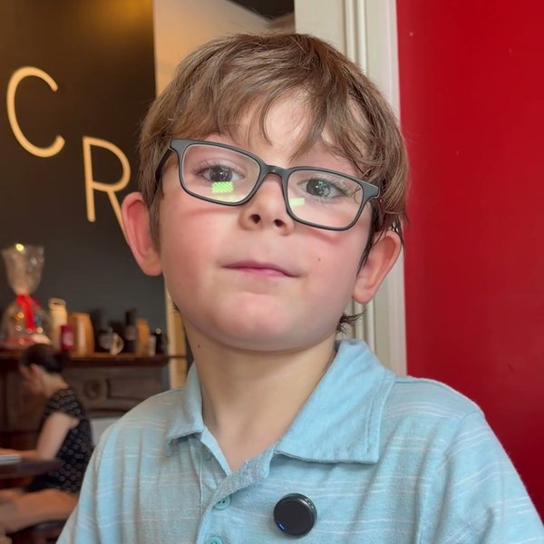 Philip, age seven, in glasses and a light blue polo, looking at the camera over a white coffee mug at CR Coffee Shop