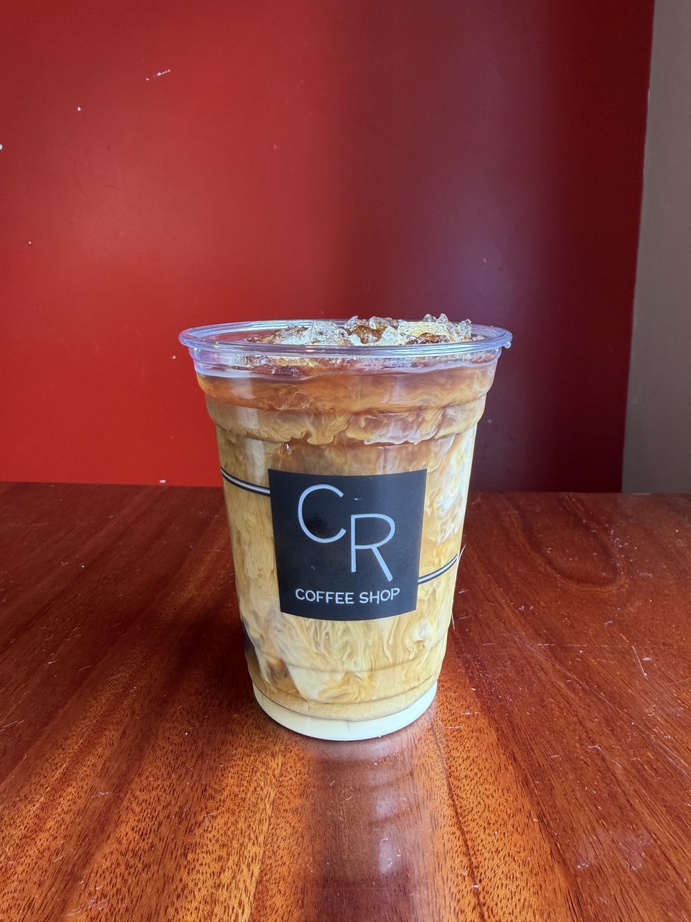A finished cold brew poured over ice in a clear CR Coffee Shop cup, with dark coffee and milk swirled together through the cup