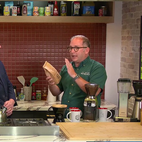 Kevin Pedeaux in the Fox 8 Kitchen holding up a bag of CR coffee beside a burr grinder, CR mugs, and a drip machine