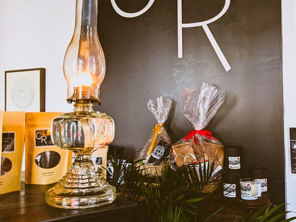 CR Coffee Shop gift bundles wrapped in cellophane beside bags of coffee and a vintage oil lamp
